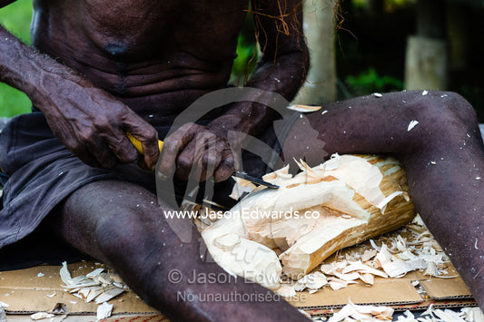 The weathered hands and skin of a man carving traditional wooden tribal figures. Agats, Asmat Regency, Papua, Indonesia