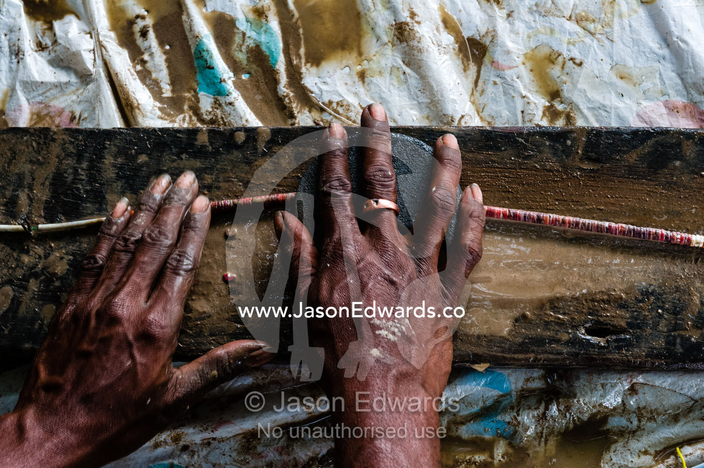 A woman's hands using a piece of flat stone to grind rough edges from a coral necklace. Samarai Island, Orangerie Bay, Milne Bay Province, Papua New Guinea