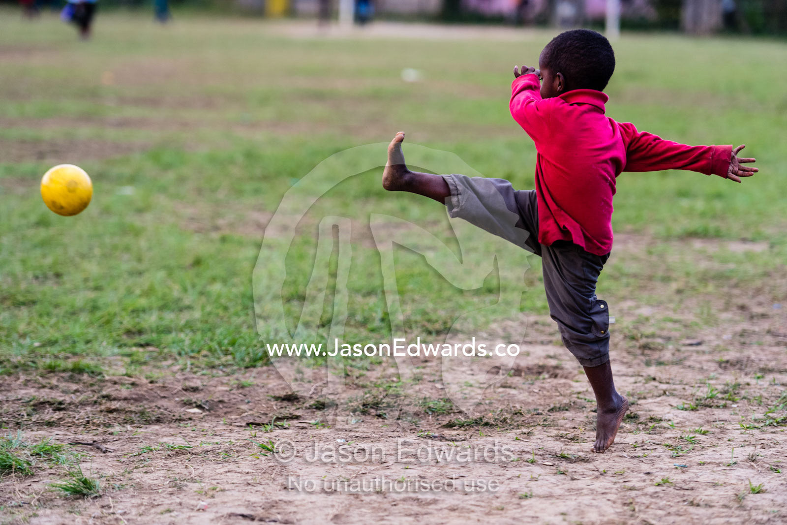 A small boy kicking a bright yellow soccer football in a village game. Andasibe, Madagascar