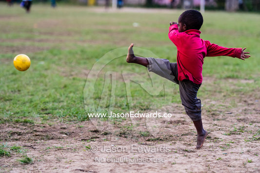 A small boy kicking a bright yellow soccer football in a village game. Andasibe, Madagascar