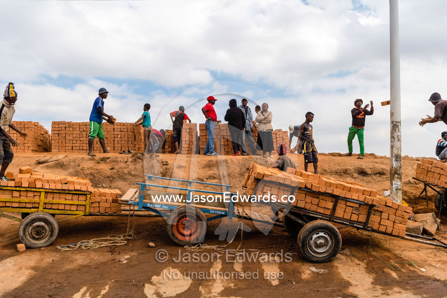 Men in a foundry loading handmade bricks onto trolleys for delivery for construction. Antananarivo, Madagascar