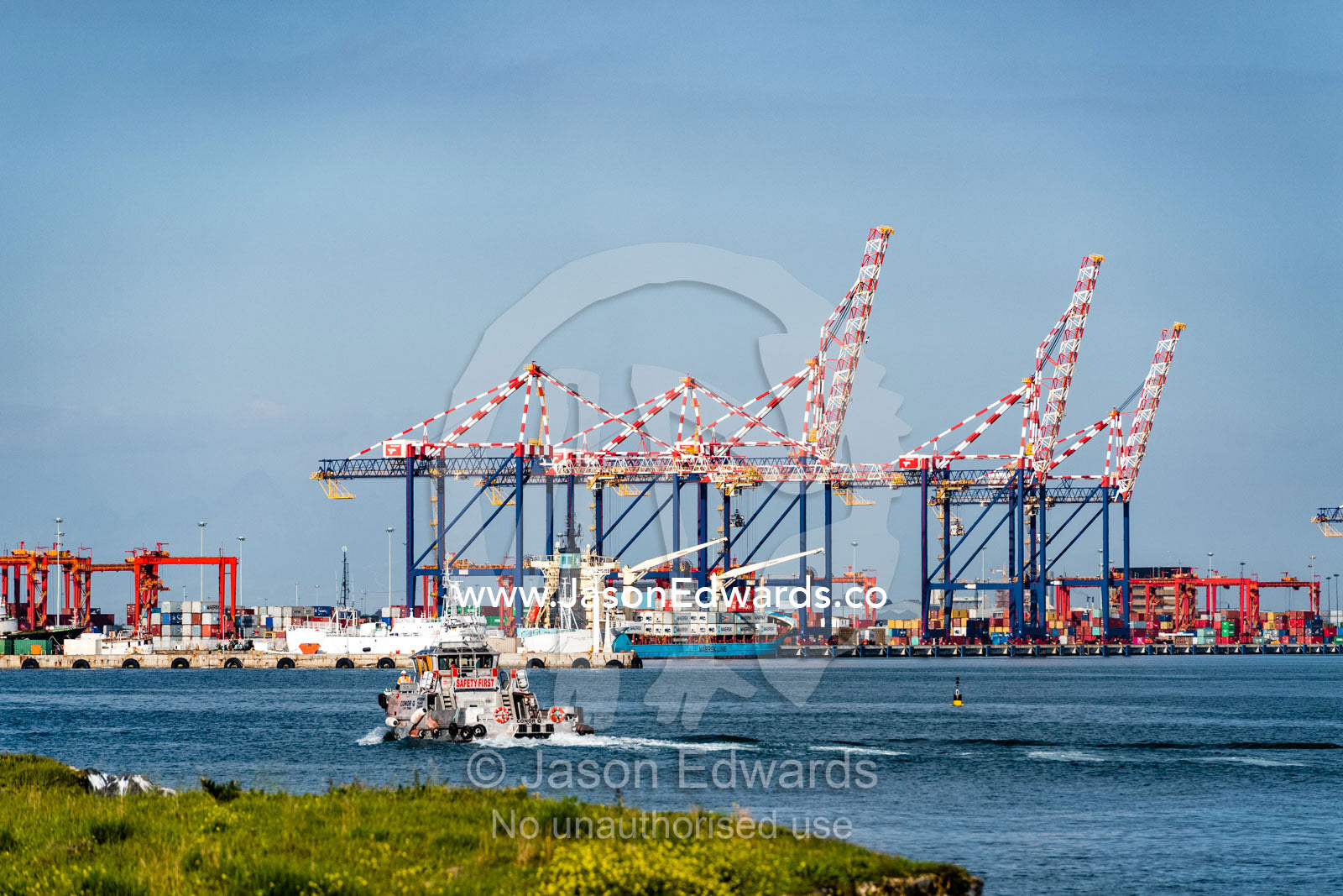A tug boat sails towards a container ship port and cranes loading cargo for transportation. Cape Town, Western Cape, South Africa