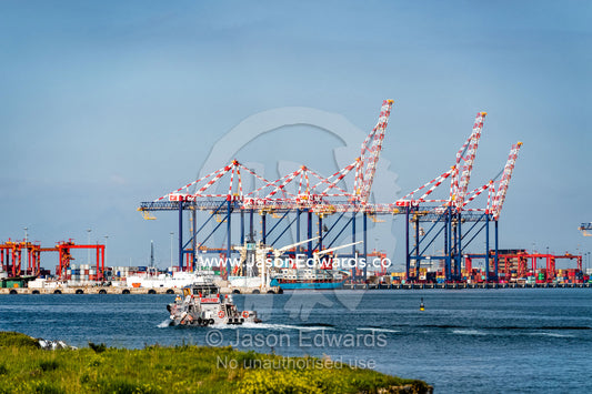 A tug boat sails towards a container ship port and cranes loading cargo for transportation. Cape Town, Western Cape, South Africa