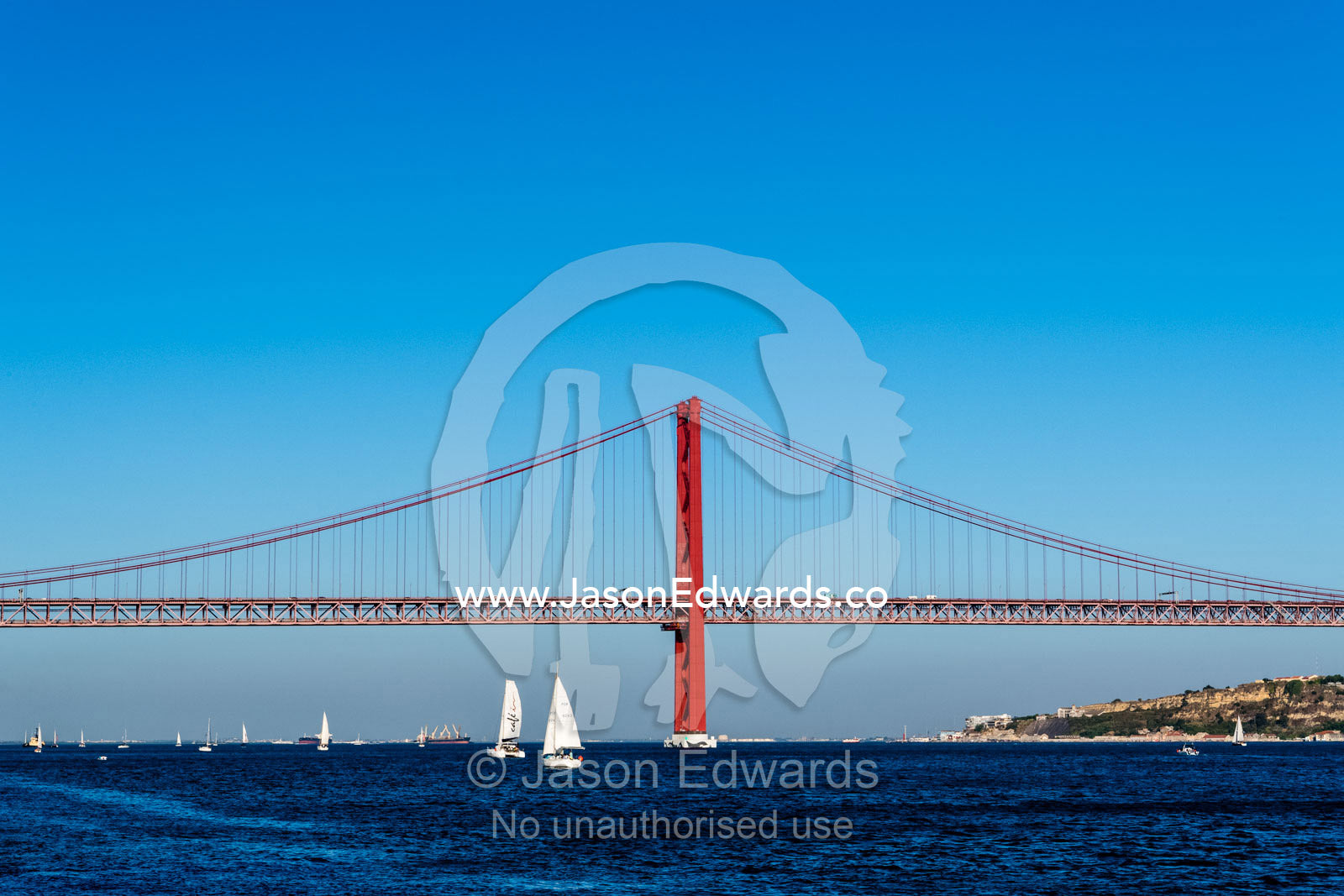 Yachts sail beneath the 25 de Abril Bridge, a suspension bridge connecting Lisbon to Almada. Lisbon, Lisboa, Portugal.