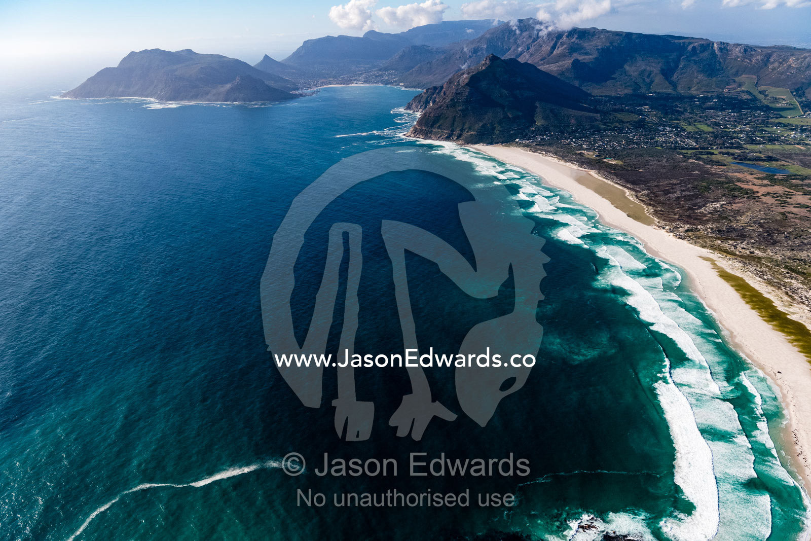 Waves peel along a sweeping sand beach beneath rugged mountains. Table Mountain National Park, South Africa