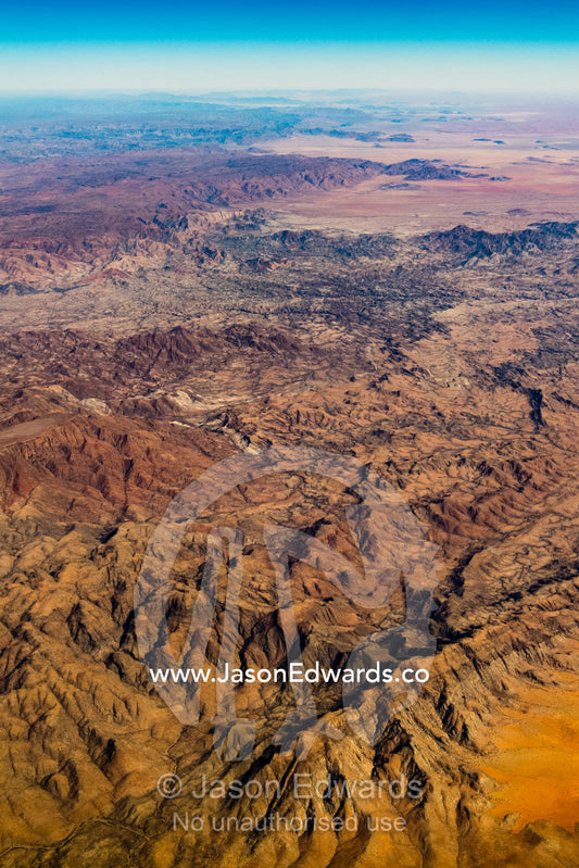An aerial view of a vast baking desert mountain range with valleys carved by erosion. Walvis Bay, Namibia