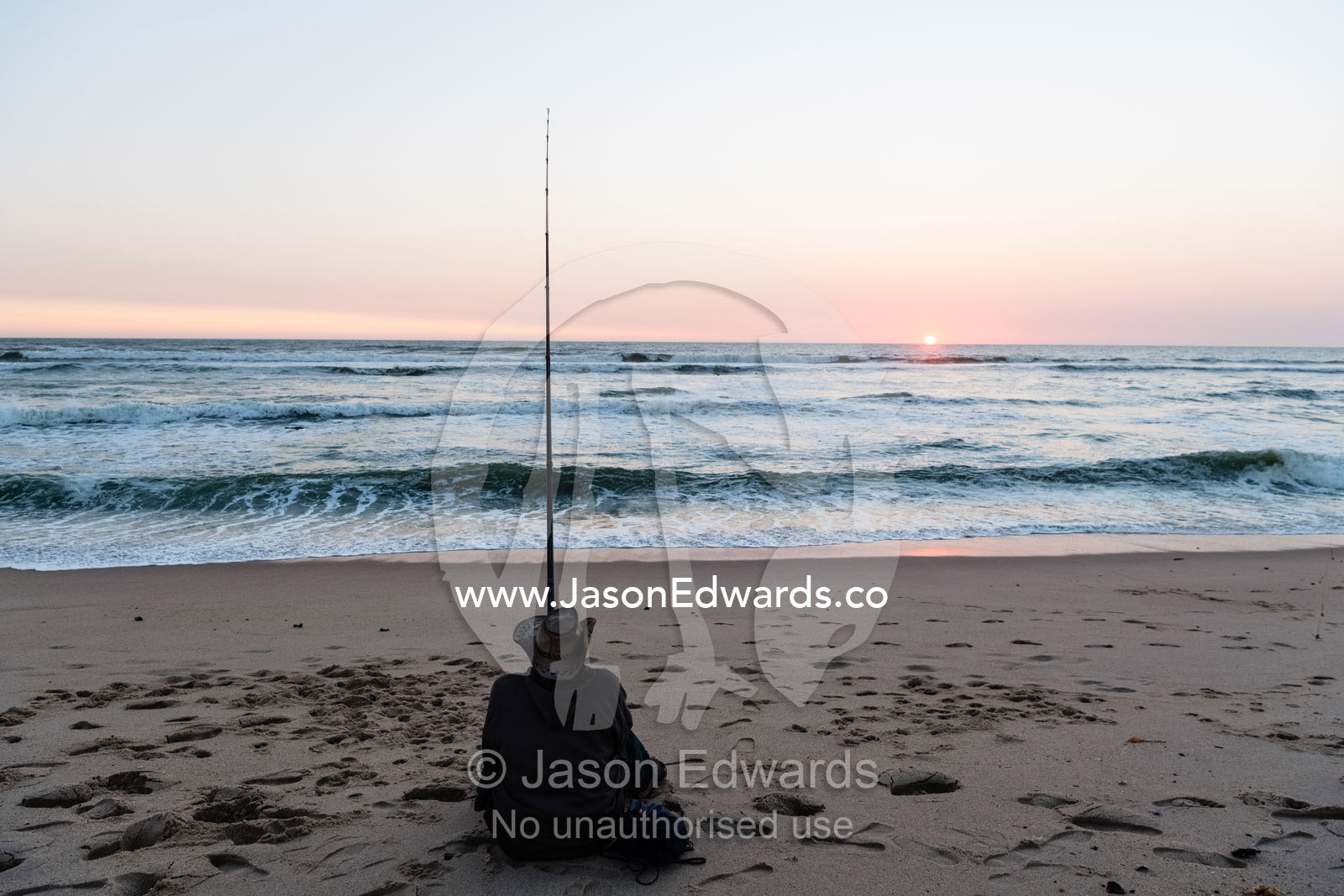 A solitary fisherman using a surf fishing rod to catch fish at sunset. Swakopmund, Namibia