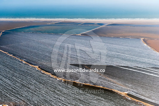 An aerial view of wind howling across the surface of coastal salt evaporation ponds. Namib Desert, Diamond Coast, Skeleton Coast, Namib-Naukluft National Park, Namibia