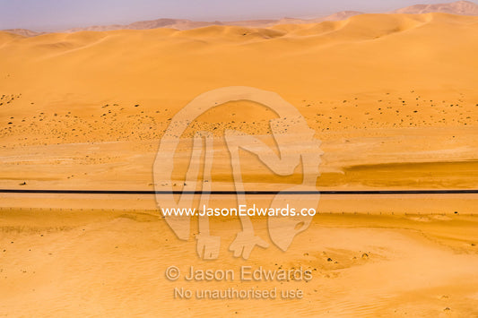 A black bitumen highway dissects a red-ochre sand dune in the desert. Namib-Naukluft National Park, Namibia