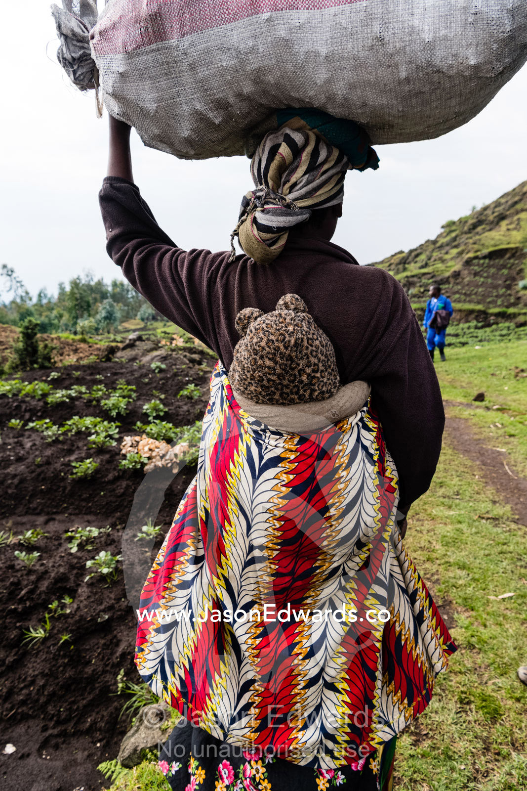 A mother with a baby in a papoose and a load of organic vegetables on her head. Ruhengeri, Rwanda