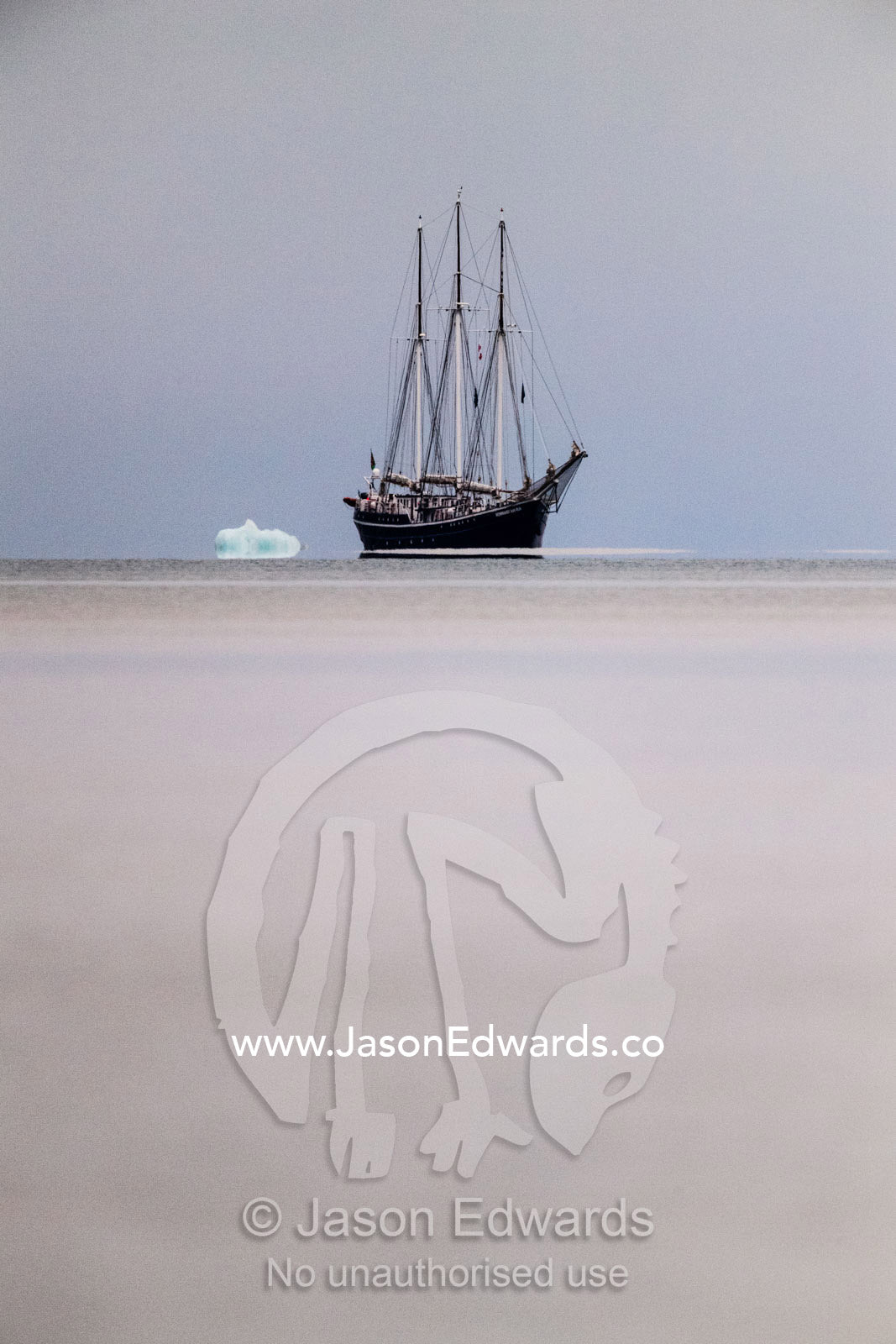 A Tall Ship Schooner moored on the horizon near an iceberg. Vikingbukt, Viking Bay, Vikingbukta, Scoresby Sound, Greenland