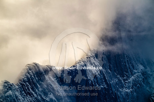 A storm consumes the sheer ridge line of an arctic mountain. Mudderbugt, Milne Land, Grundtvigskirken, Bjorne Islands, Scoresby Sound, Greenland