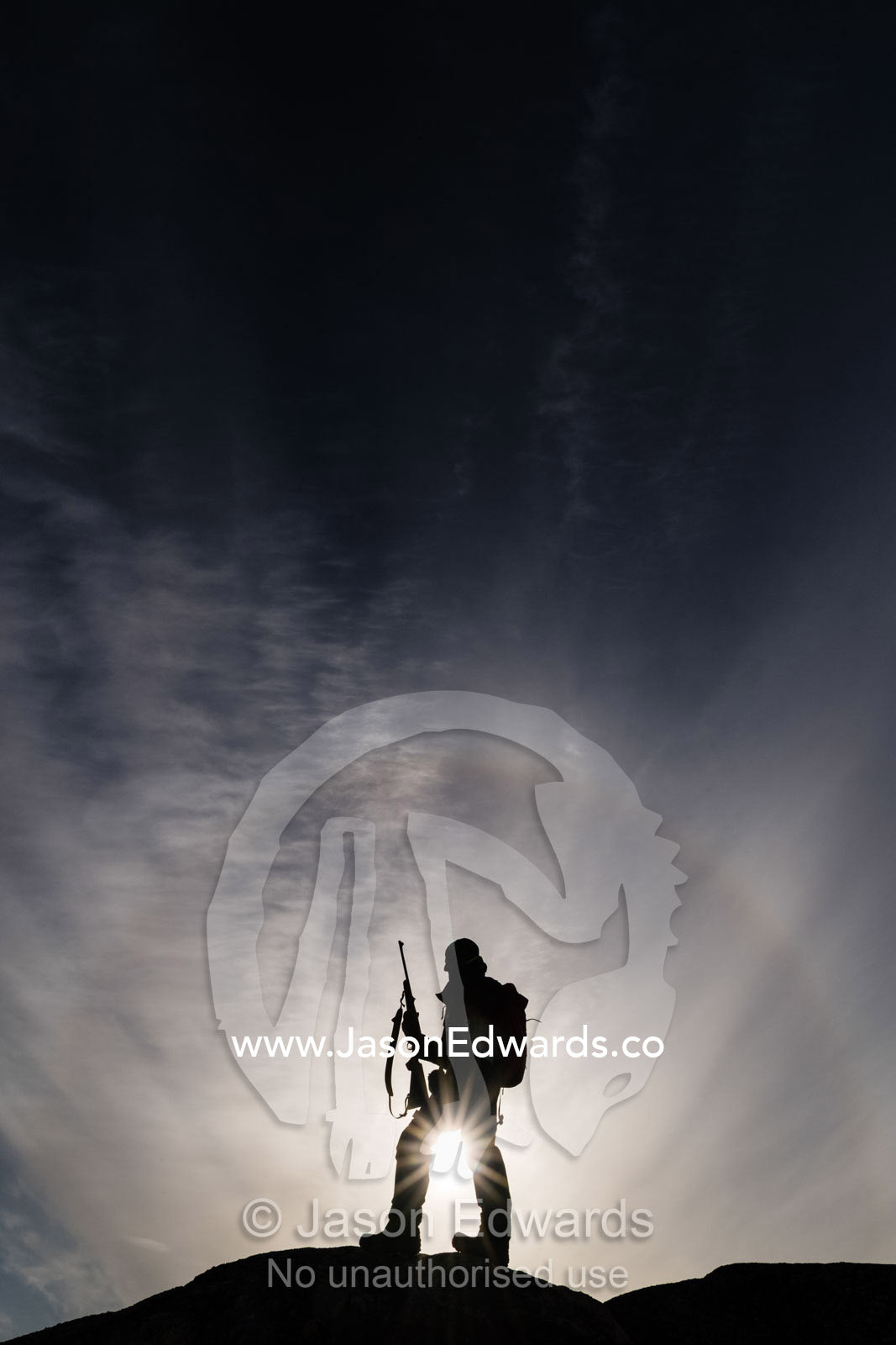An arctic guide silhouette on a mountain top with a hunting rifle surrounded by a halo. Milne Land, Jytte Havn, Bjorne Islands, Scoresby Sound, Greenland