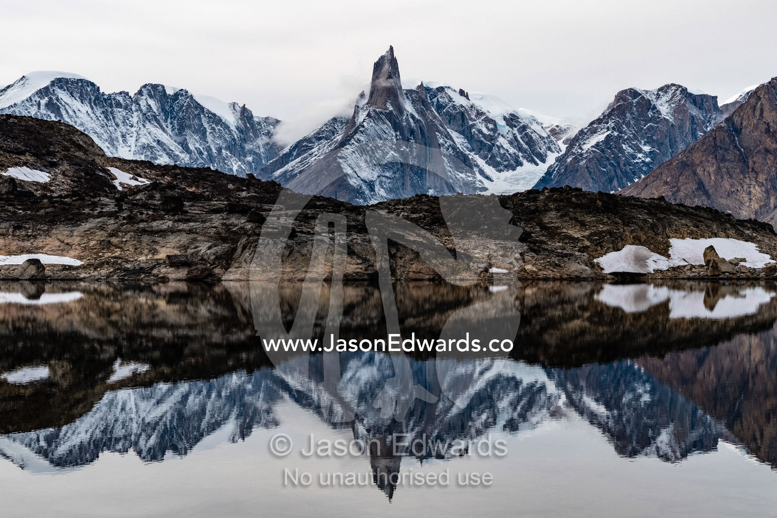 A jagged spire of rock shrouded in ice and snow reflecting in a still arctic pool. O Fjord, Island Fjord, Milne Lan, Grundtvigskirken, Bjorne Islands, Scoresby Sound, Greenland