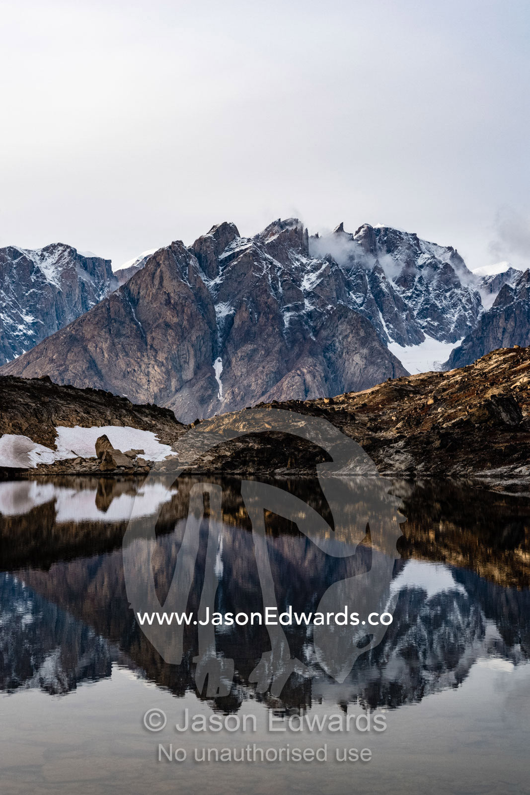 A jagged spire of rock shrouded in ice and snow reflecting in a still arctic pool. O Fjord, Island Fjord, Milne Lan, Bjorne Islands, Scoresby Sound, Greenland