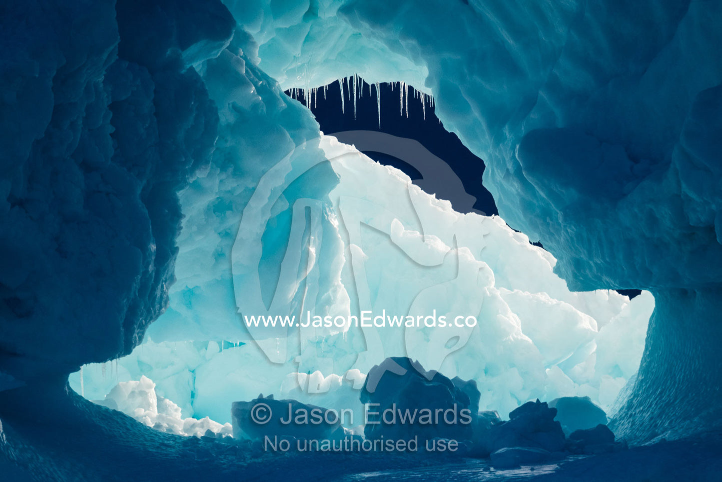 An tunnel of ice with icicle teeth carves it's way through an iceberg. Scoresby Sound, Greenland
