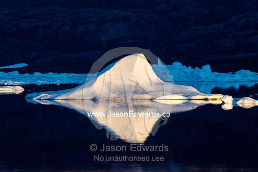 An iceberg shaped like a pyramid reflecting in the dark, still waters of an arctic fjord. Rolinge Glacier, Rode Fjord, Scoresby Sound, Greenland