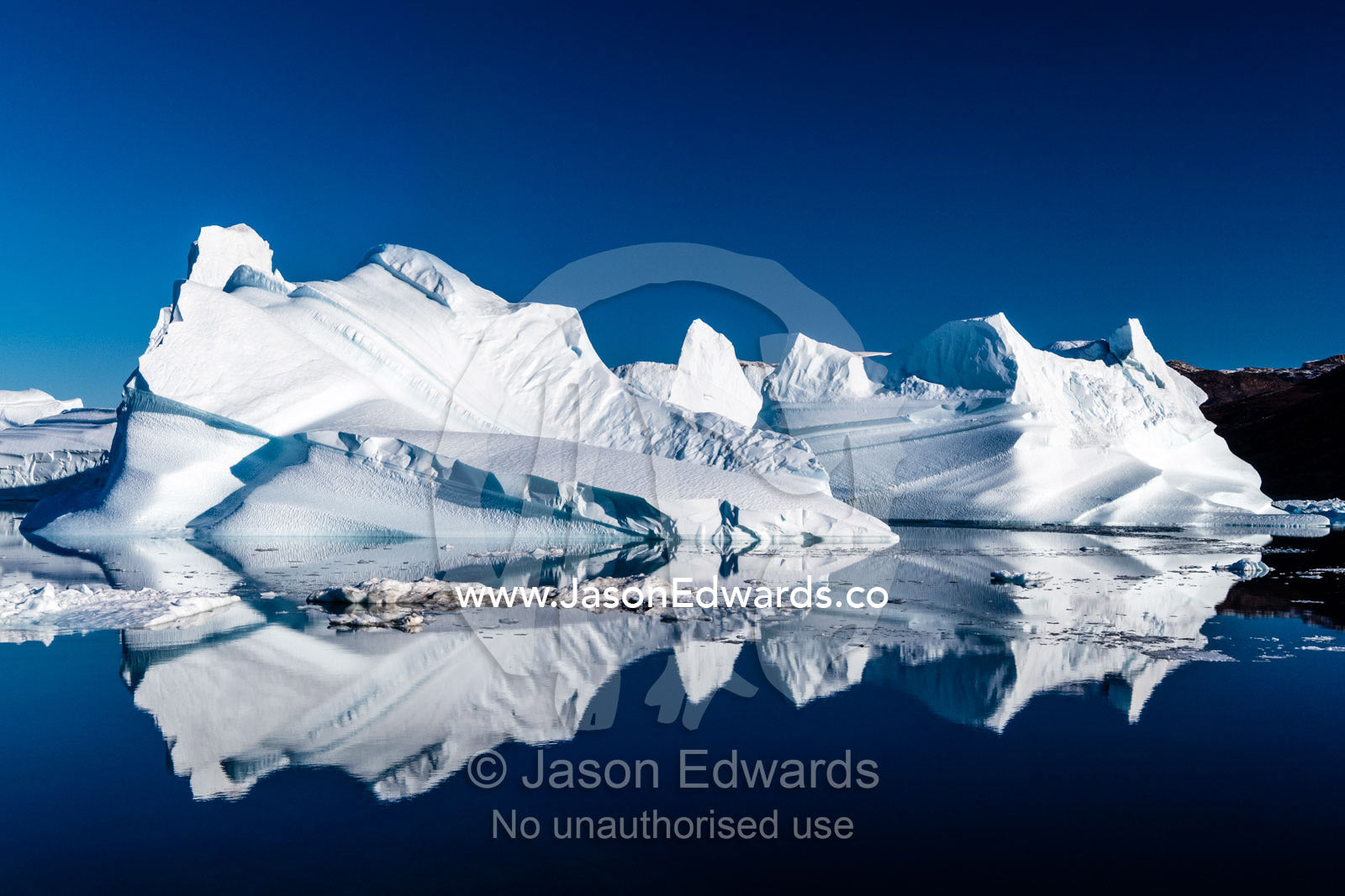 Sculptured mountains of ice carved by erosion reflecting in an Iceberg Graveyard. Milne Land, Rode Island, Red Island, Rode Fj, Scoresby Sound, Greenland
