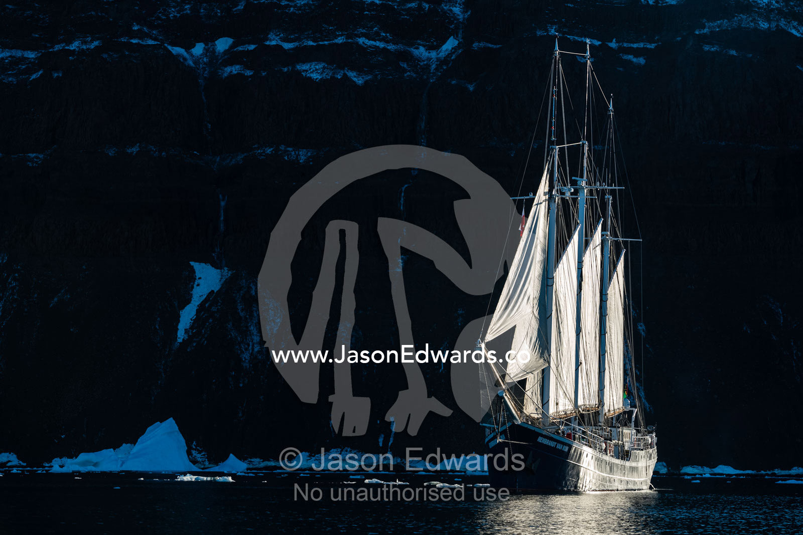 A Tall Ship Schooner sailing along a rugged arctic coastline. Milne Land, Vikingbukt, Viking Bay, Scoresby Sound, Greenland