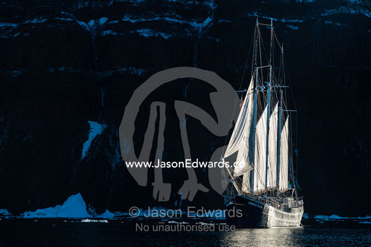A Tall Ship Schooner sailing along a rugged arctic coastline. Milne Land, Vikingbukt, Viking Bay, Scoresby Sound, Greenland
