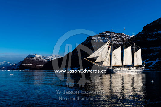 A Tall Ship Schooner sailing along a rugged arctic coastline. Milne Land, Vikingbukt, Viking Bay, Scoresby Sound, Greenland