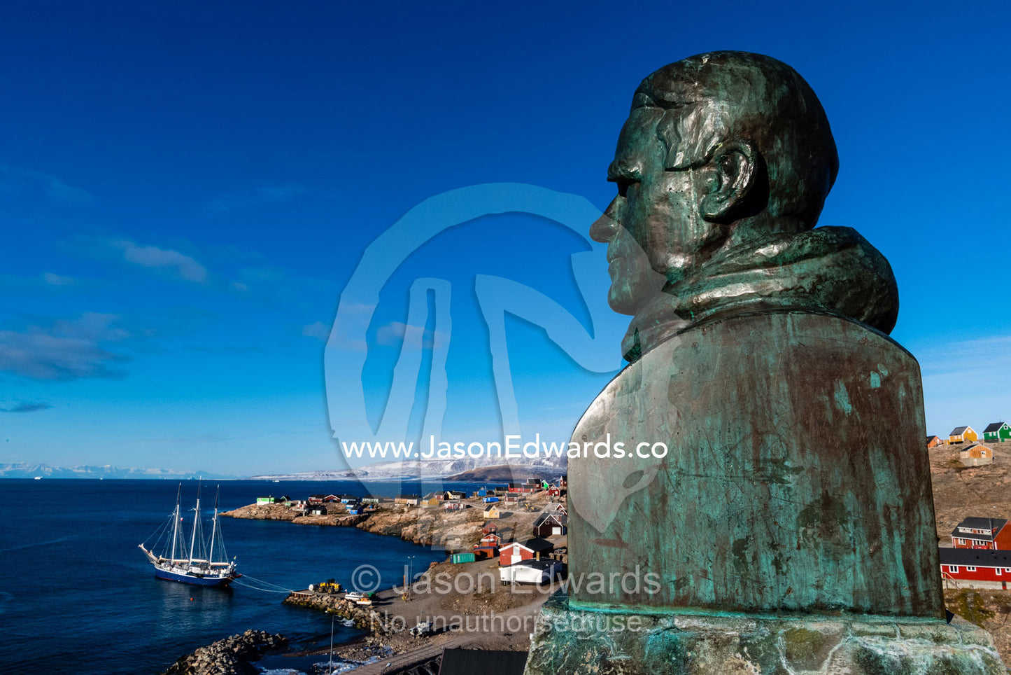 A bronze bust statue of Ejnar Mikkelsen overlooks the harbour of an inuit village. Sermersooq Municipality, Ittoqqottoormiit, Scoresby Sound, Greenland