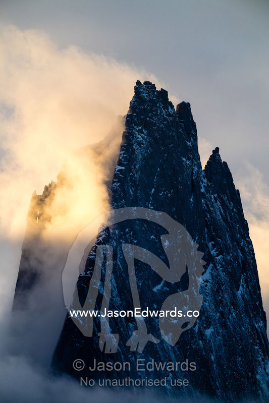 Sunset illuminates mist and cloud trapped inside a jagged mountain spire. Mudderbugt, Milne Land, Grundtvigskirken, Bjorne Islands, Scoresby Sound, Greenland