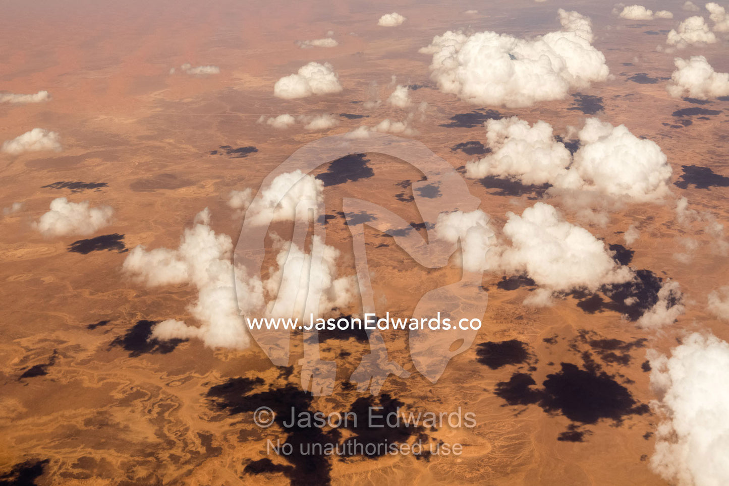Tufts of fluffy white clouds cast shadows over the red ochre sands of the Sahara desert. Sahara Desert, Tunisia