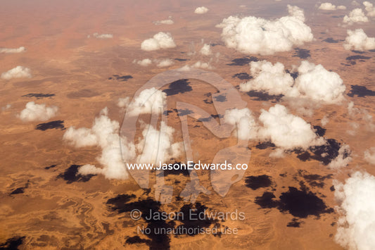 Tufts of fluffy white clouds cast shadows over the red ochre sands of the Sahara desert. Sahara Desert, Tunisia