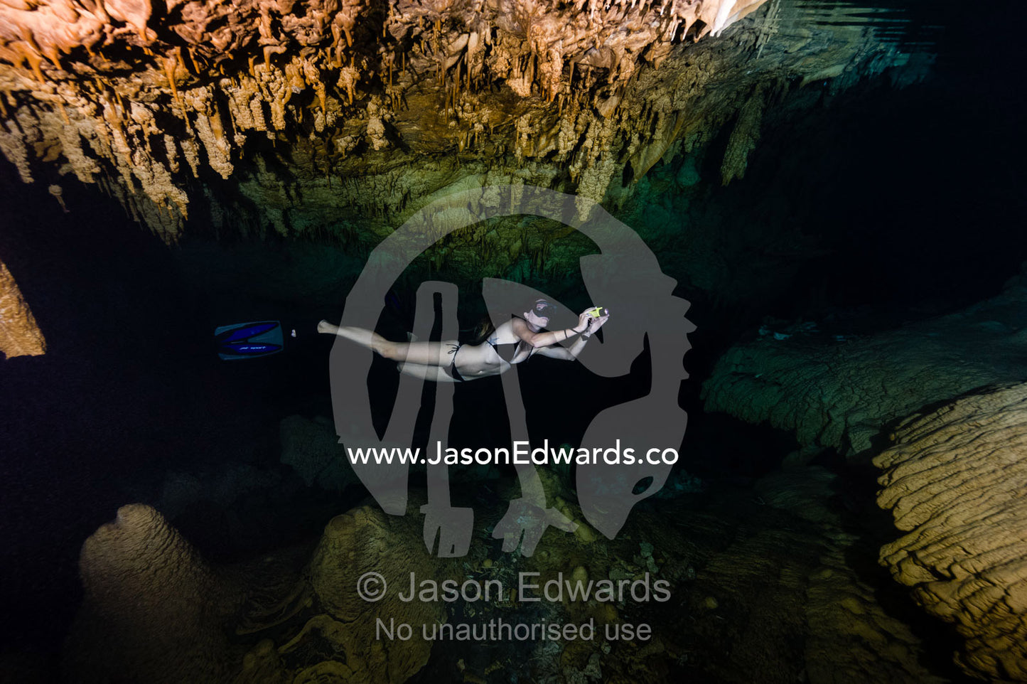 A freediver explores limestone stalactites hanging from the ceiling in a submerged cave. Makatea Atoll, Tuamotu Archipelago, French Polynesia