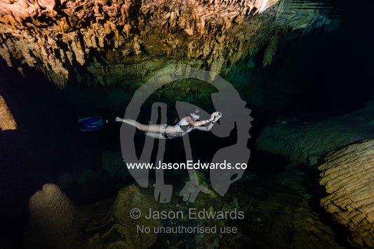 A freediver explores limestone stalactites hanging from the ceiling in a submerged cave. Makatea Atoll, Tuamotu Archipelago, French Polynesia