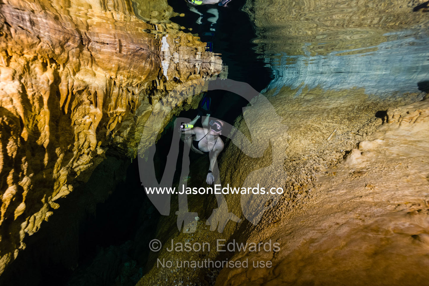 A freediver explores limestone stalactites hanging from the ceiling in a submerged cave. Makatea Atoll, Tuamotu Archipelago, French Polynesia
