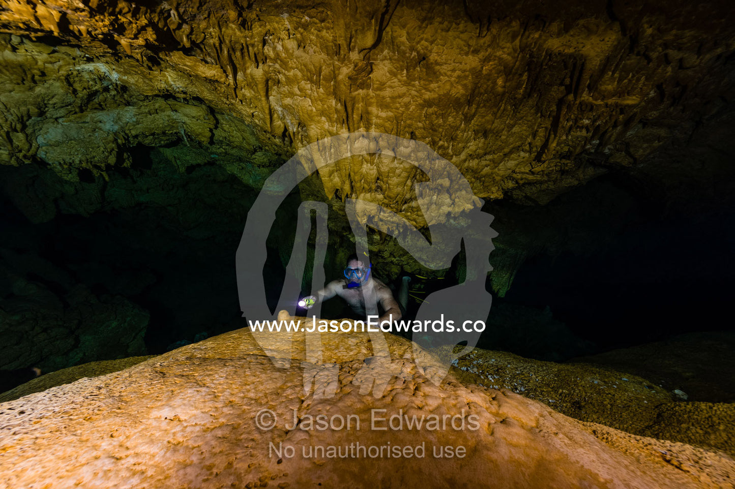 A freediver explores an underwater limestone cave with a torch. Makatea Atoll, Tuamotu Archipelago, French Polynesia