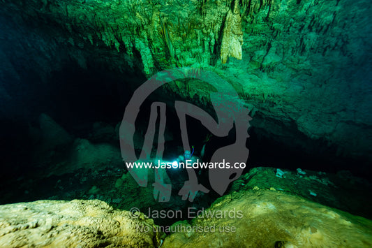 A freediver explores an underwater limestone cave with a torch. Makatea Atoll, Tuamotu Archipelago, French Polynesia