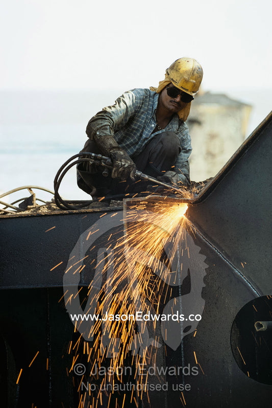 A worker cuts apart an old ship to reclaim the steel for recycling. Alang, India.