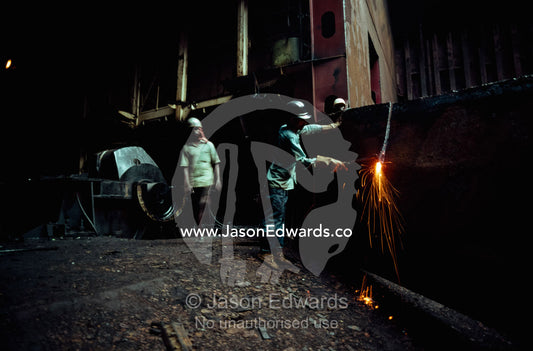 Without eye protection, a worker uses a torch to dismantle a ship. Alang, India.