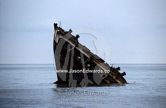 The stern of a dismantled ship emerges from the sea. Alang, India.