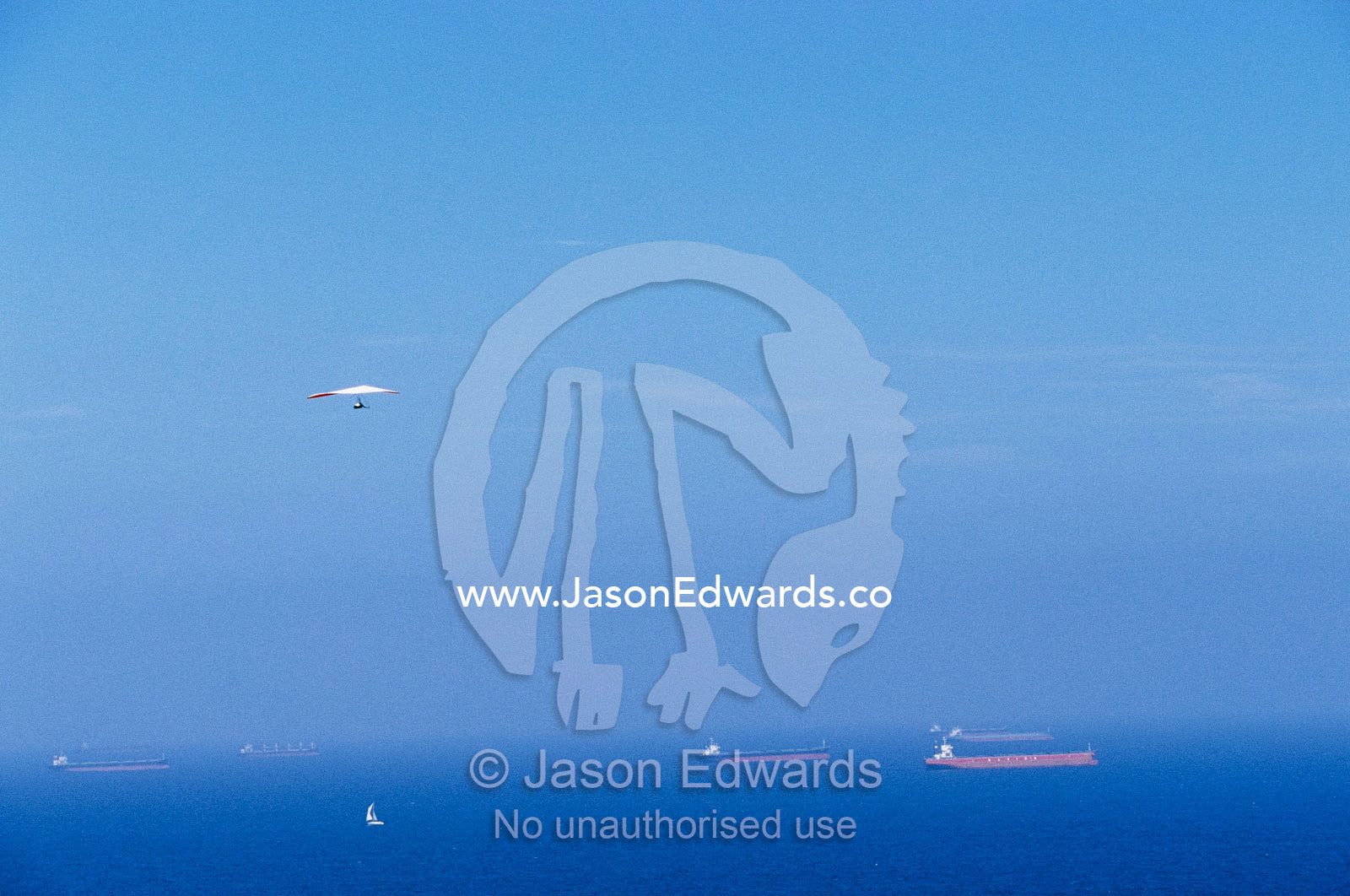 A hang glider in blue sky over a sea dotted with ships and boats. Merewether, New South Wales, Australia.