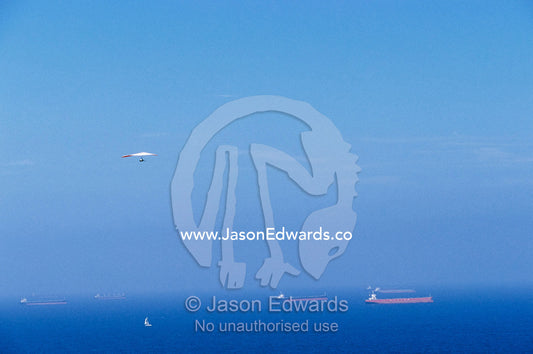 A hang glider in blue sky over a sea dotted with ships and boats. Merewether, New South Wales, Australia.