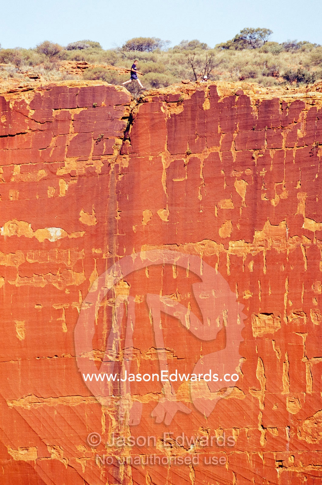 A hiker leaps over a rift in the Kings Canyon cliff face wall. Watarrka National Park, Northern Territory, Australia.