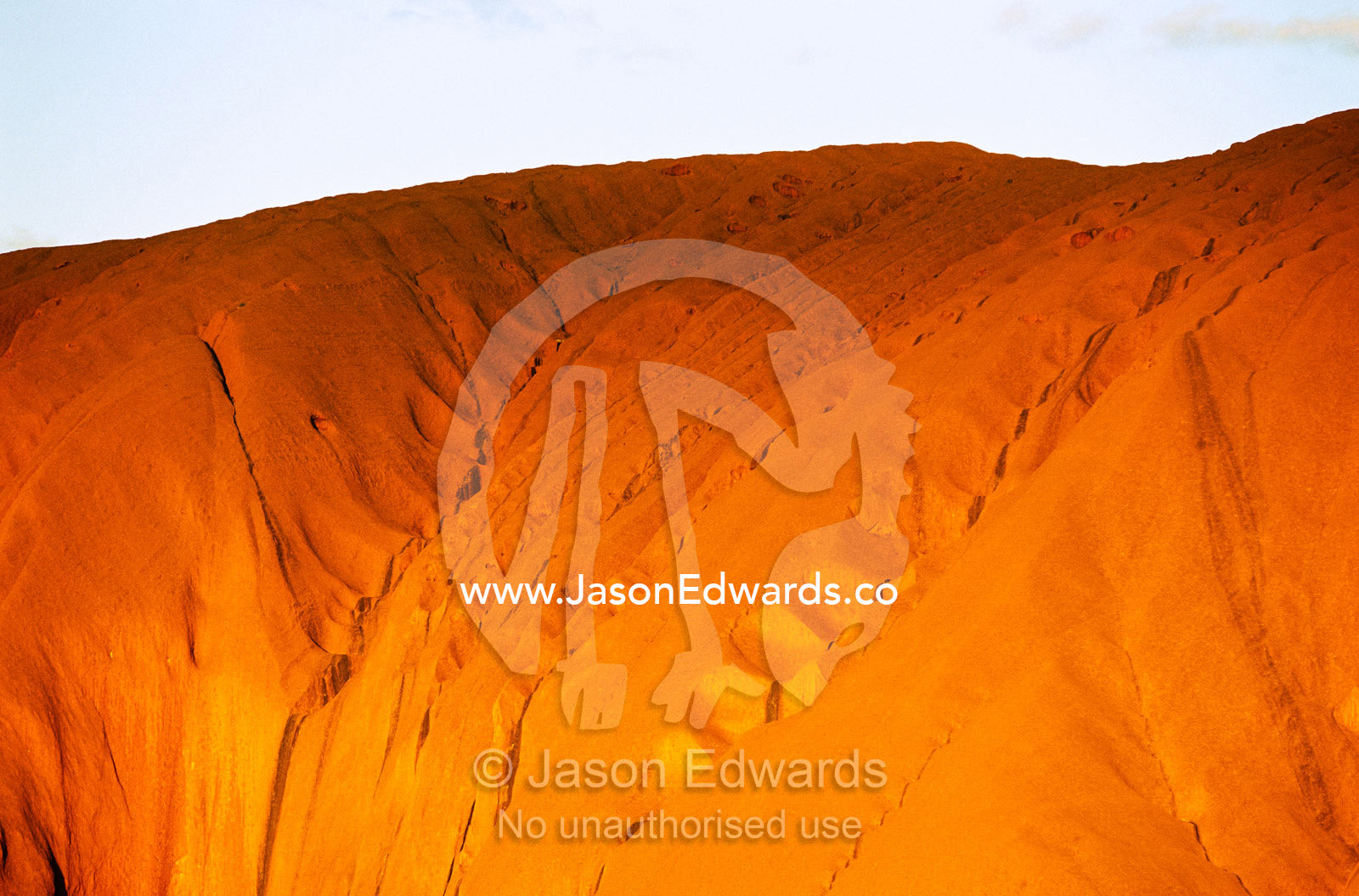 The setting sun casts a golden glow on an Uluru rock formation. Uluru National Park, Northern Territory, Australia.