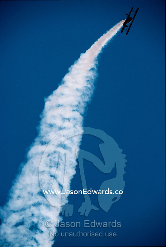 A stunt bi-plane in a steep climb trails smoke at the Avalon Airshow. Victoria, Australia.