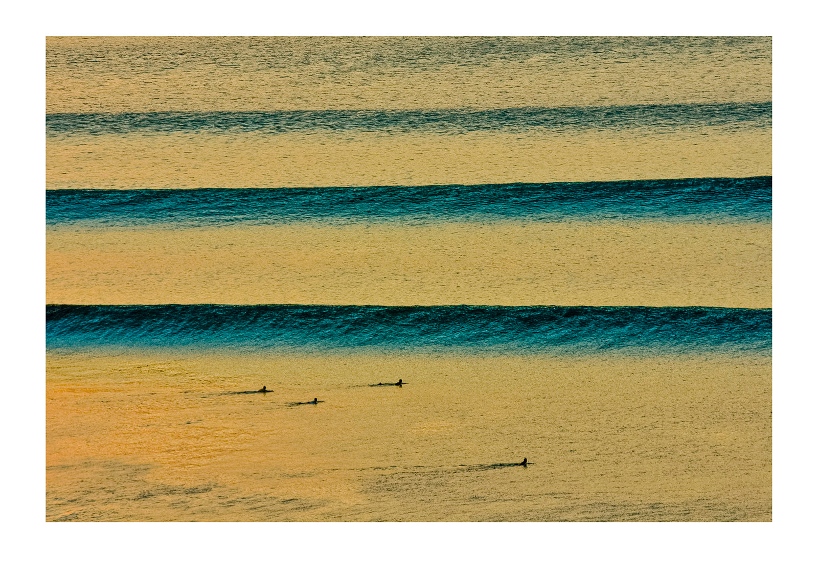 Surfers await beautiful clean sunset waves as they roll in over a reef Impossibles, Bukit Peninsula, Bali, Indonesia.