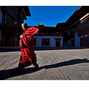 A brisk wind catches the flaming-red robes of a Buddhist monk as he strides purposefully between prayers in a Himalayan valley in Bhutan.