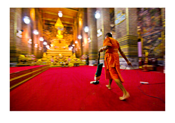 A Buddhist Monk vacuums the chapel's red carpet after evening prayer. Wat Pho, Temple of the Reclining Buddha, Wat Chetuphon, Phra Nakhon District, Rattanakosin District, Bangkok, Thailand.