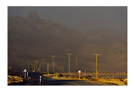 A sunray pierces a storm and lights electricity poles running through a mountain pass. Abyaneh village, Abyaneh, Barzrud Rural District, Natanz County, Isfahan Province, Islamic Republic of Iran.
