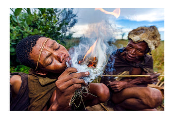 A San hunter blowing on a small fire he started using sticks. Kalahari Desert, Botswana.