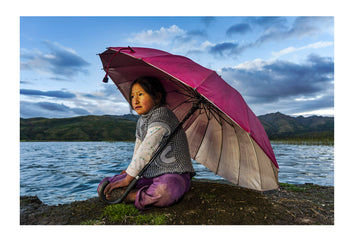 A young girl watches the sun fall behind an active volcano on the Andes Mountains, the last rays illuminating her features beneath her umbrella. Peru.