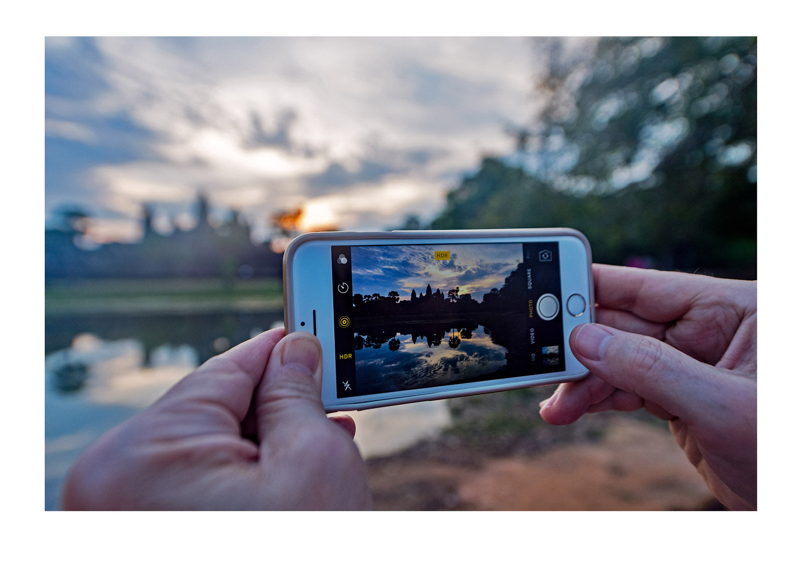 A tourist takes a photo of the ancient ruins of Angkor Wat at dawn using a smart phone. Angkor Wat, Siem Reap, Cambodia.