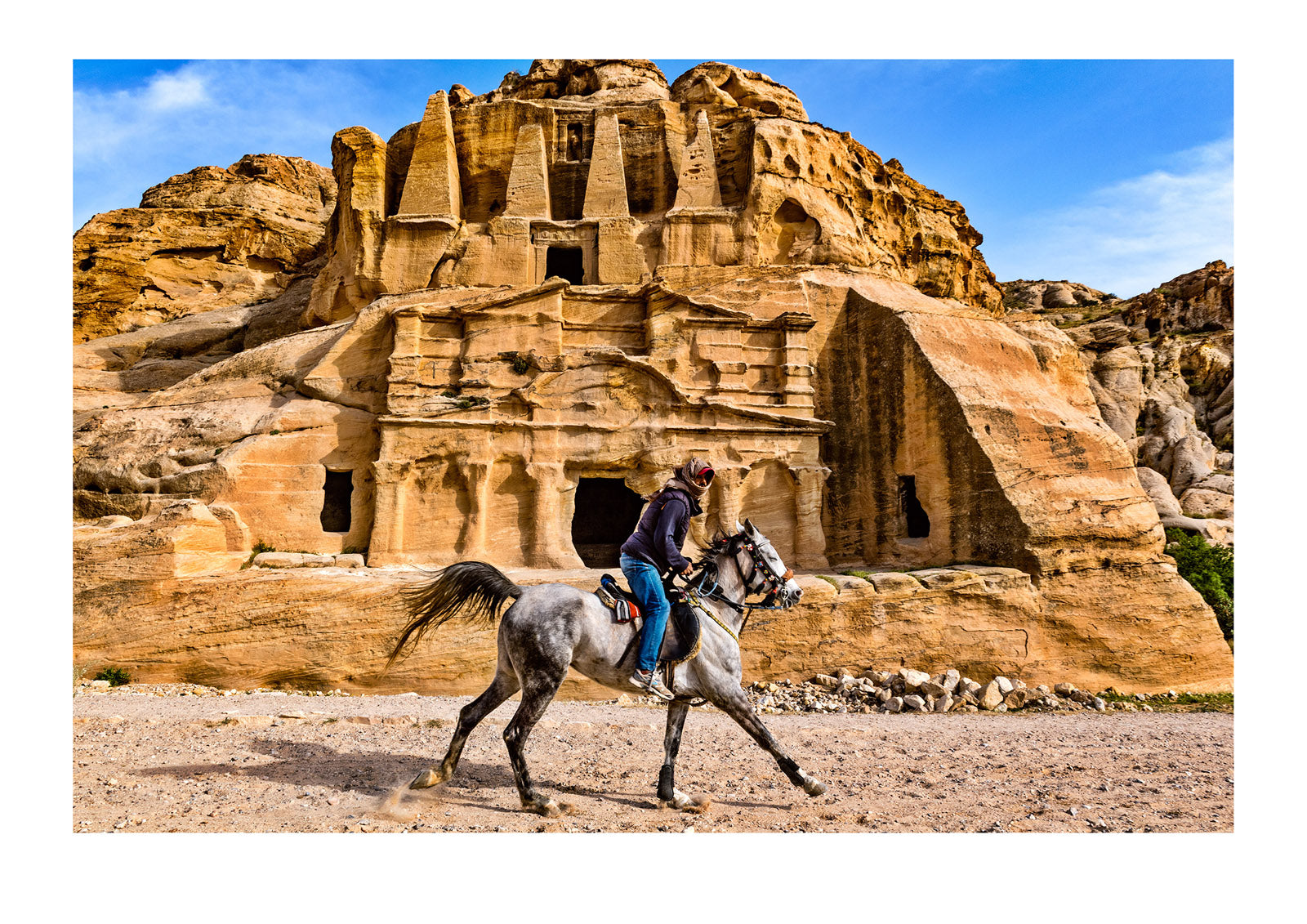 A Bedouin man galloping on a horse past the ancient ruins of the Obelisk Tomb, above, and Bab as-Siq Triclinium, below, rock-cut architecture, 1st century AD. Petra, The Lost City of Petra, Jordan